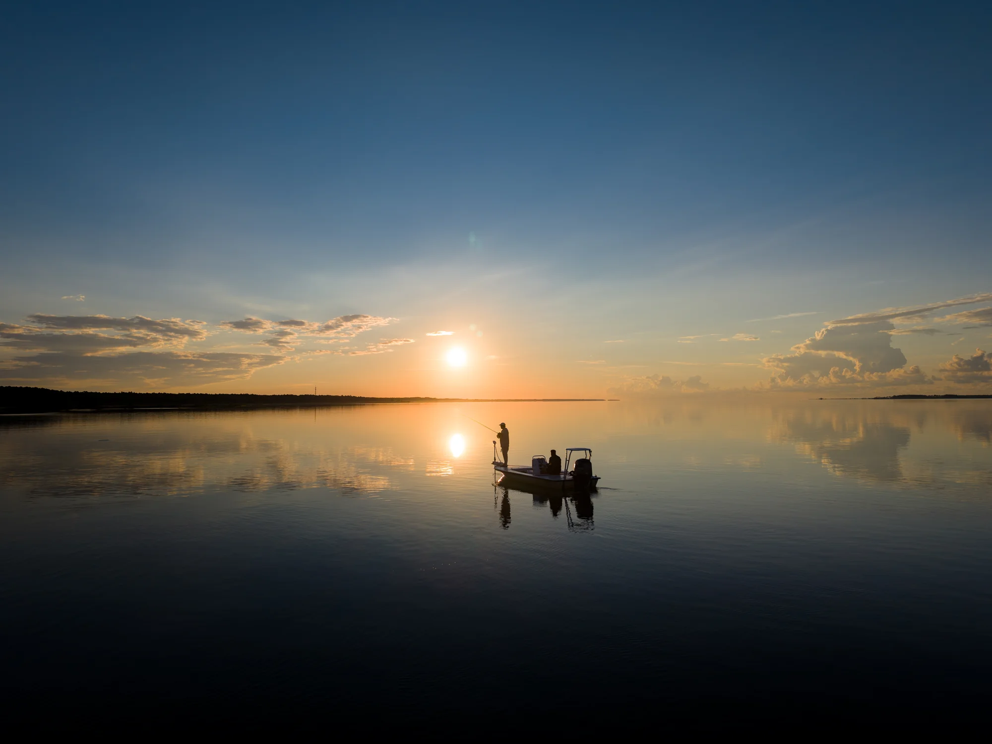 Drone photo at sunrise over glass-calm St. Joseph Bay near Port St. Joe FL — two anglers fishing from a flats boat, by JandyLucho